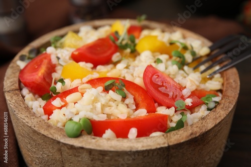 Cooked bulgur with vegetables in bowl on table, closeup