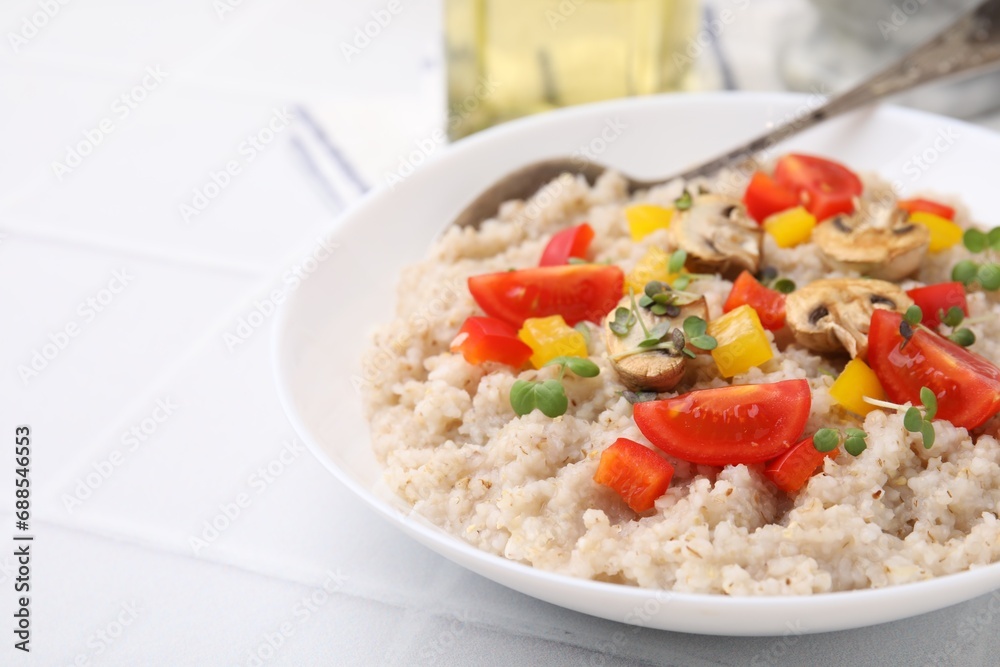 Delicious barley porridge with vegetables and microgreens in bowl on white table, closeup