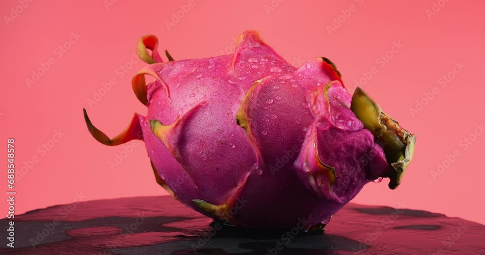 Dragon fruit pitahaya in drops of water on a black stone serving board isolated on a pink background. Dragon fruit pitahaya in drops of water on a black stone serving board isolated on a pink background.
