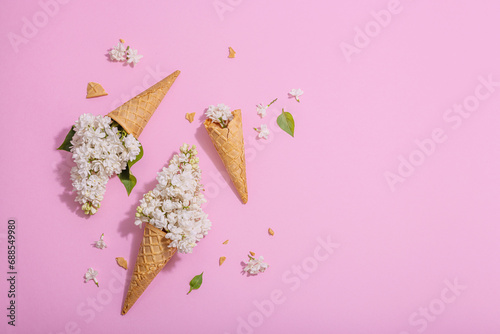 White lilac flowers in waffle ice cream cones on pink background. Flat lay