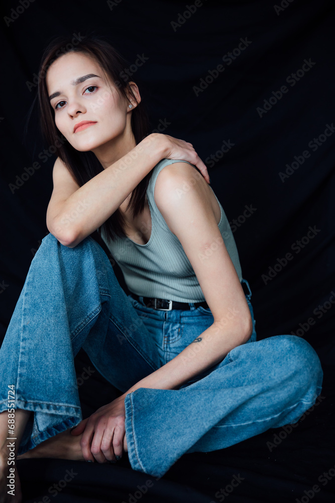 Naklejka premium Beautiful young slender woman in jeans sitting