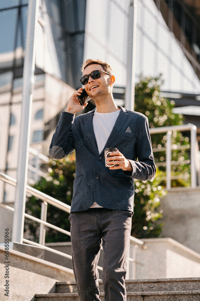 Walking cheerful office worker talking on smartphone outdoors and drink cup of coffee to go. Walking cheerful office worker talking on smartphone outdoors and drink cup of coffee to go.