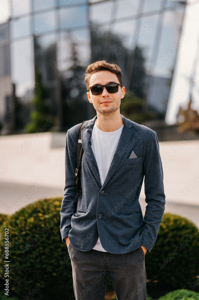Vertical portrait of young man in casual looking at camera outdoors near new buildings.