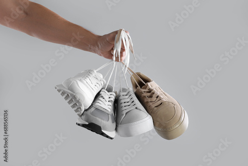 Man holding different sneakers on light grey background, closeup
