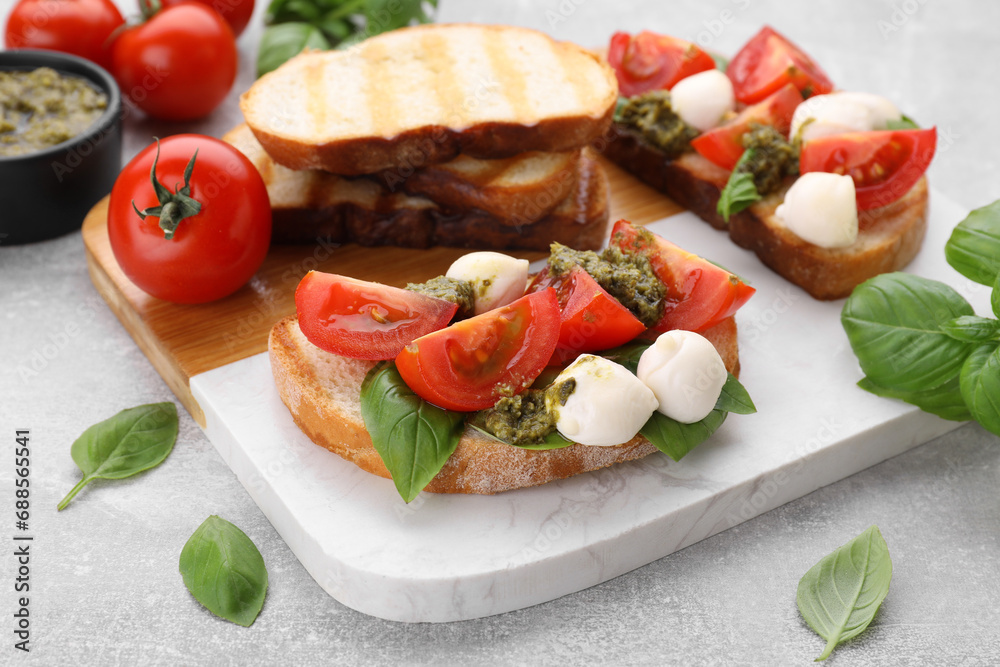 Delicious Caprese sandwiches with mozzarella, tomatoes, basil and pesto sauce on light grey table