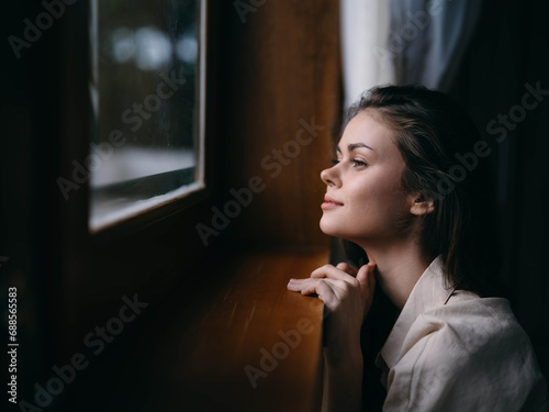Portrait of young woman at home by window with wooden frame, autumn mood, cozy lifestyle, sleepy weather, relax on chair.
