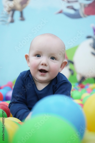 Portrait of a cute smiling eared baby among colorful balls. Cute baby in the children's room. Close-up portrait. Vertical photo.