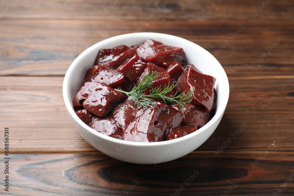 Cut raw beef liver with dill on wooden table, closeup