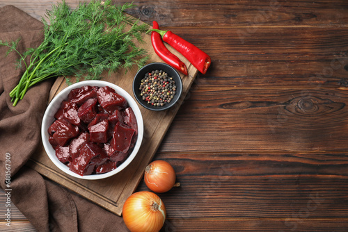 Cut raw beef liver with onions, spices, chili peppers and dill on wooden table, flat lay. Space for text photo