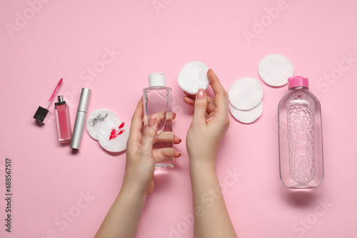 Woman with makeup remover, cotton pads, cosmetic product, lip gloss and mascara on pink background, top view