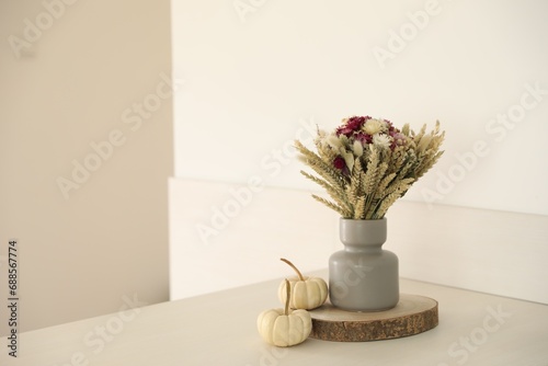 Beautiful bouquet of dry flowers in vase and small pumpkins on white table indoors, space for text