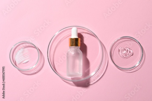 Bottle of cosmetic serum and petri dishes with samples on pink background, flat lay