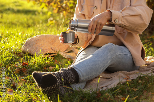 Picnic time. Woman pouring tea from thermos into cup lid on green grass outdoors, closeup