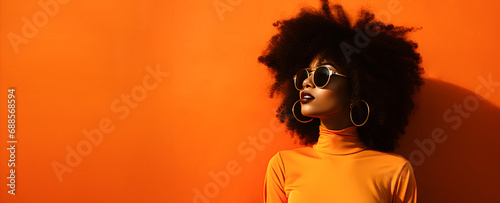 Cool and modern black woman wearing sunglasses on orange banner background. photo