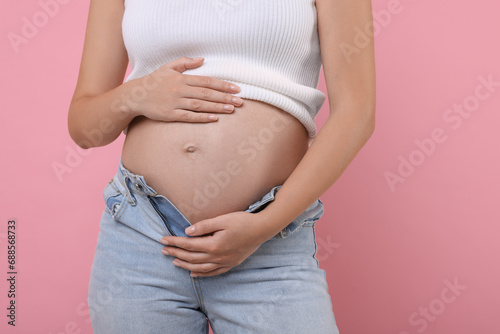 Pregnant woman in jeans on pink background, closeup