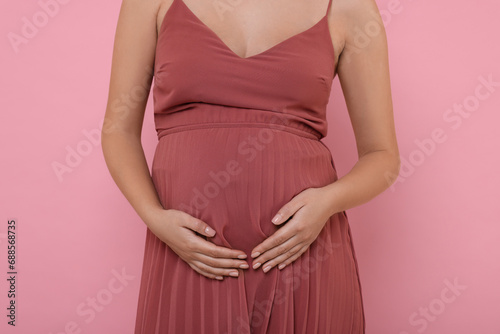 Pregnant woman in dress on pink background, closeup
