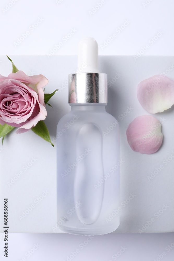 Bottle of cosmetic serum, beautiful rose flower and petals on white background,top view Bottle of cosmetic serum, beautiful rose flower and petals on white background,top view
