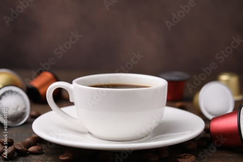 Cup of coffee, capsules and beans on table, closeup. Space for text