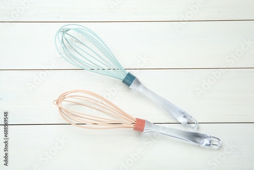 Two whisks on white wooden table  top view