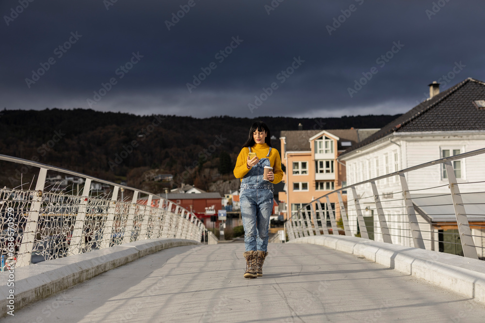 young adult woman walking through a city in Norway while looking at her cell phone