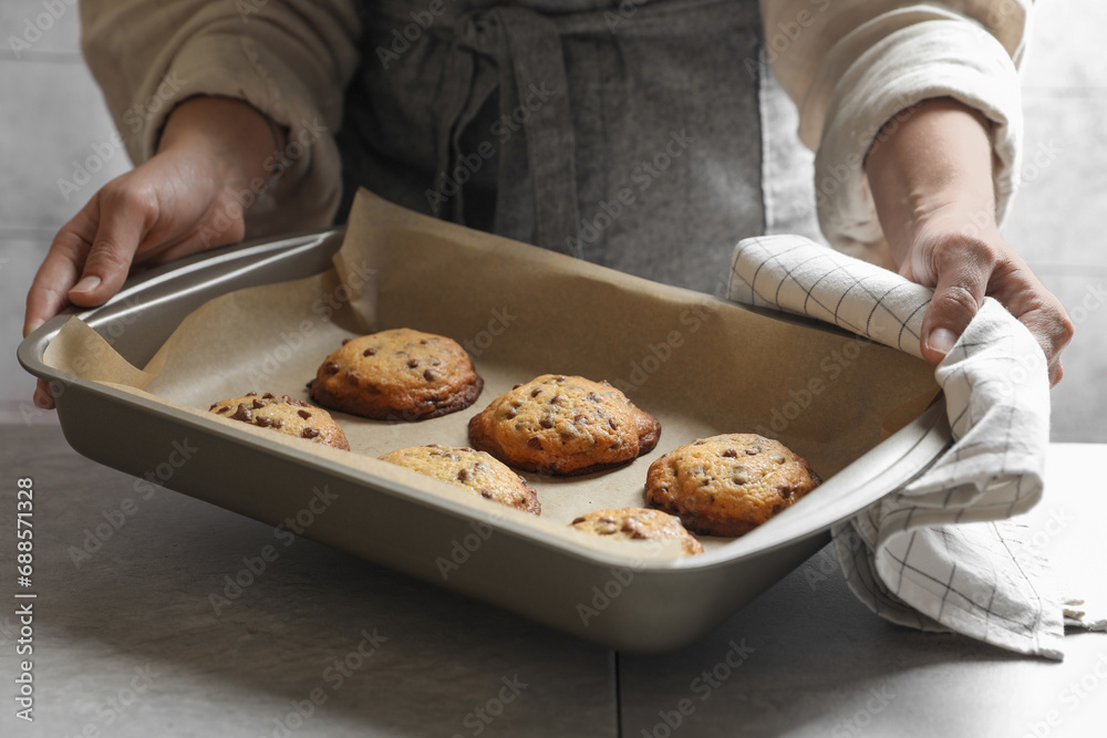 Woman putting baking pan with chocolate chip cookies on table, closeup