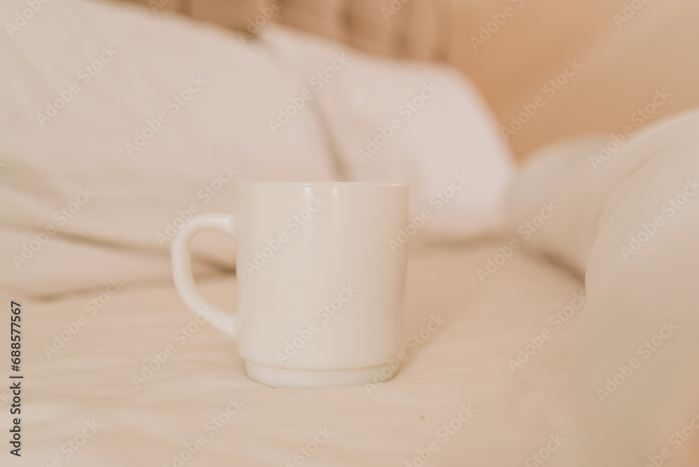 White coffee cup on the bed in sunny morning bedroom, mock up.