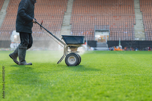 Groundsman spreads fertilizer for grass on a football pitch photo