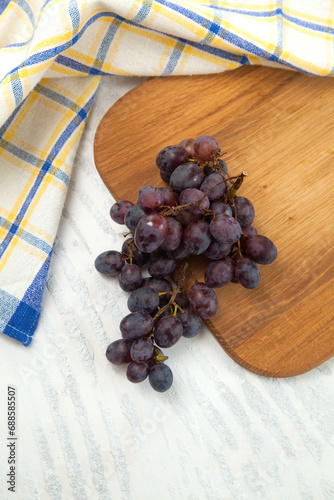 Cutting board with bunch of organic black grapes on white wooden background..