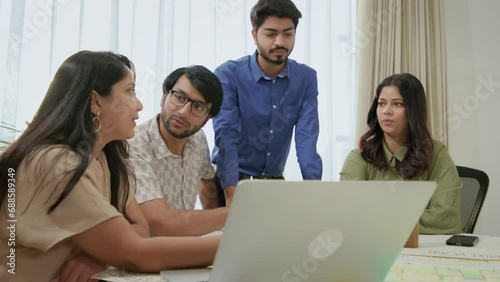 Modern mixed gender Group of young Indian Corporate entrepreneurs discussing work together at a conference table in front of laptop during business meeting in office workplace.