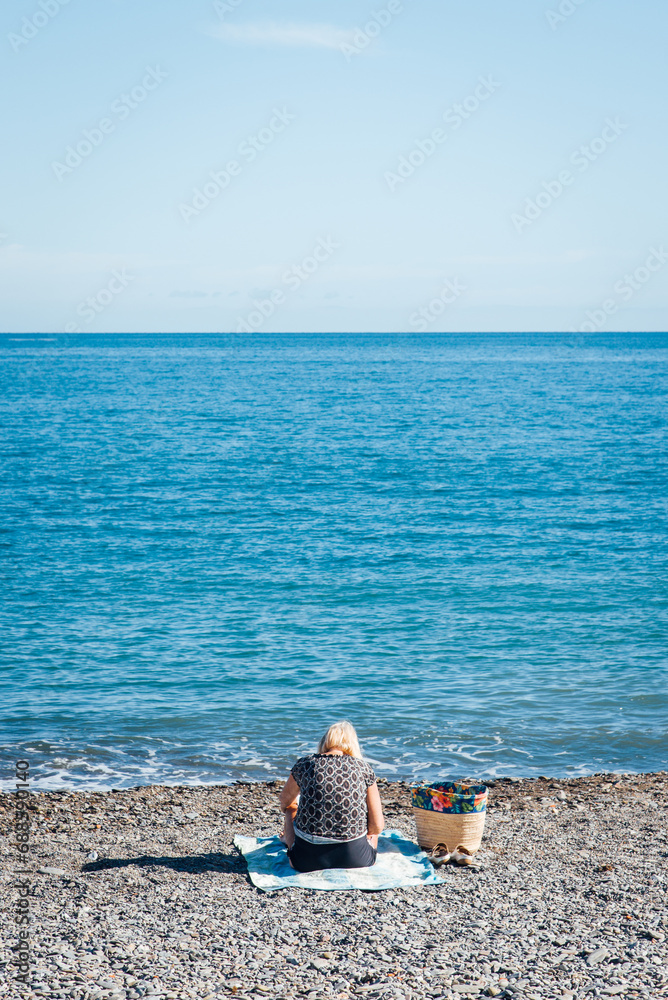 Une Femme Assise Seule Sur La Plage Face La Mer Une Personne De Dos une-femme-assise-seule-sur-la-plage-face-la-mer-une-personne-de-dos