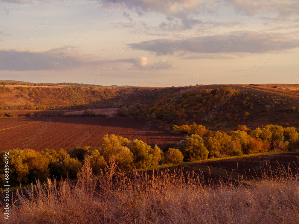 Plowed fields in a valley between hills at sunset. Autumn agronomic landscape.