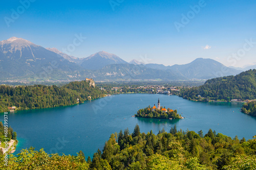 View of Lake Bled with St. Marys Church of Assumption on a small island on a sunny day. Lake with turquoise water. Slovenia, Europe. Mountains on background. Areal view from above.