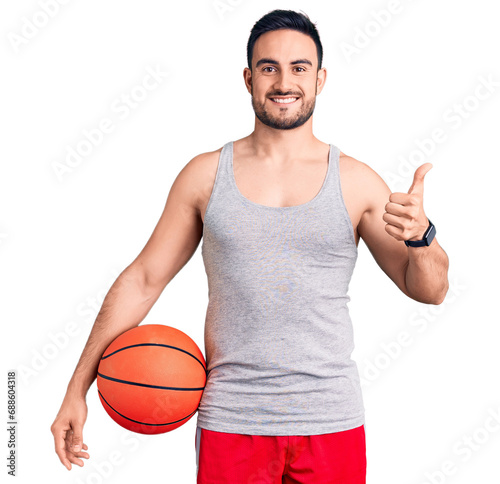 Young handsome man holding basketball ball smiling happy and positive, thumb up doing excellent and approval sign