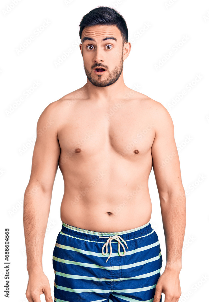 Young handsome man wearing swimwear in shock face, looking skeptical and sarcastic, surprised with open mouth Young handsome man wearing swimwear in shock face, looking skeptical and sarcastic, surprised with open mouth