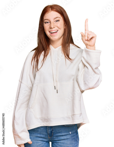 Young read head woman wearing casual sweatshirt pointing finger up with successful idea. exited and happy. number one.