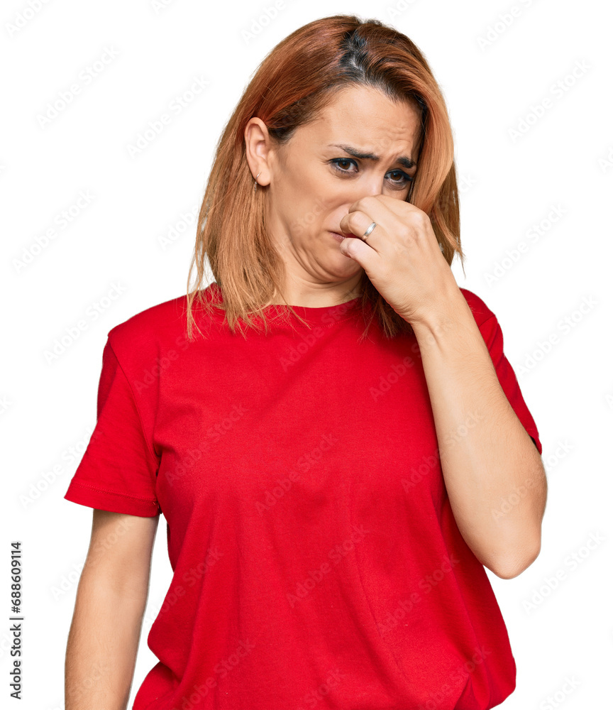 Hispanic young woman wearing casual red t shirt smelling something stinky and disgusting, intolerable smell, holding breath with fingers on nose. bad smell Hispanic young woman wearing casual red t shirt smelling something stinky and disgusting, intolerable smell, holding breath with fingers on nose. bad smell