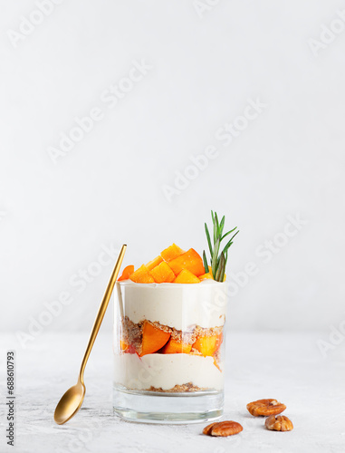 Parfait in a glass with persimmon, rosemary, pecan, whipped cream, biscuit and spoon. Healthy food, vegan, sugar, gluten and lactose free.