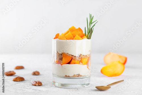 Trifle in a glass with persimmon, rosemary, pecan, whipped cream and biscuit. Healthy food, vegan, sugar, gluten and lactose free.