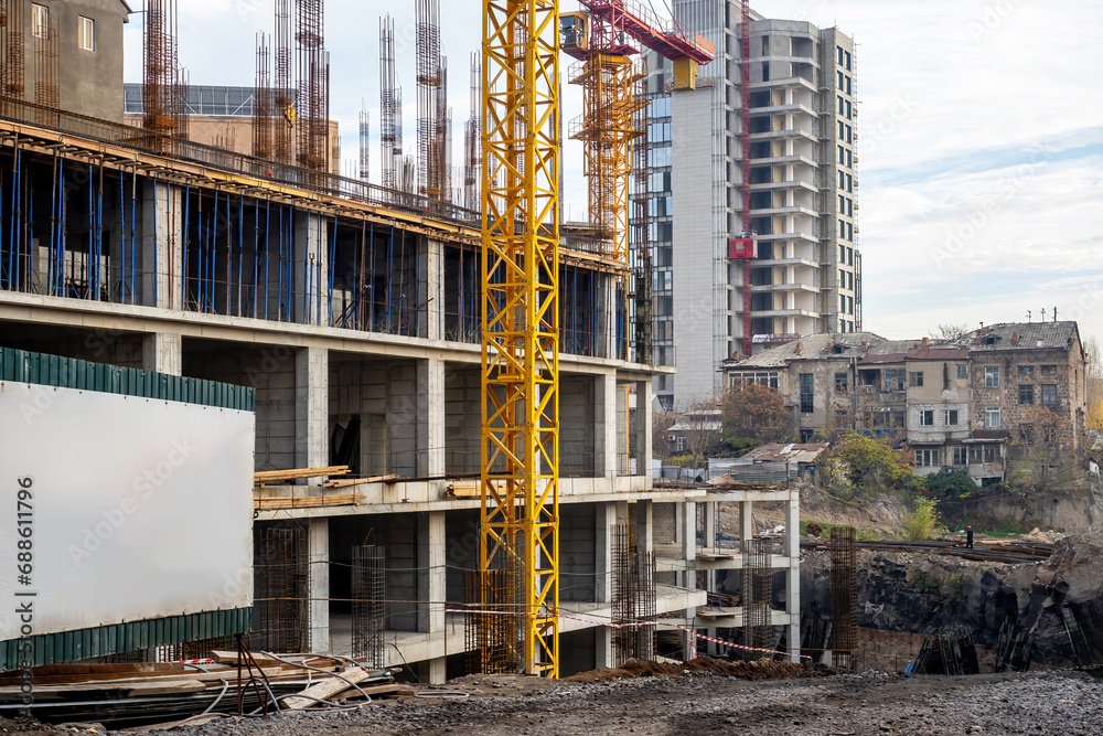 Construction of multi-storey building. Tower crane is constructing stone building. Construction site without workers. Erection of monolithic buildings. Residential area under construction