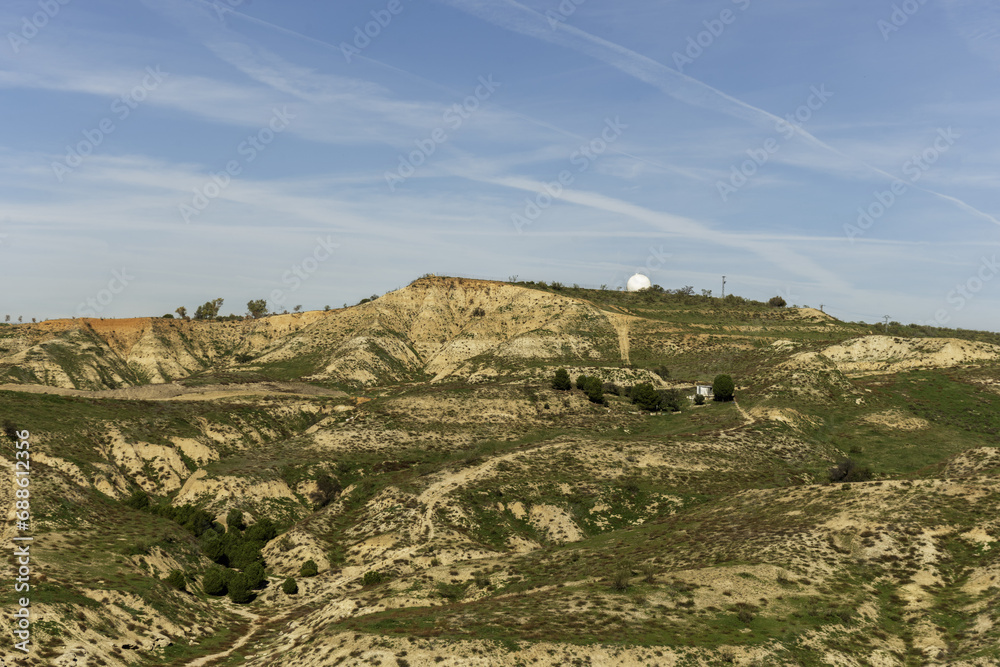 Landscape of a mountain with eroded material and a white geodesic dome covering radars