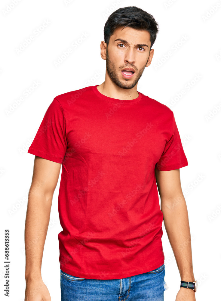 Obraz premium Young handsome man wearing casual red tshirt in shock face, looking skeptical and sarcastic, surprised with open mouth