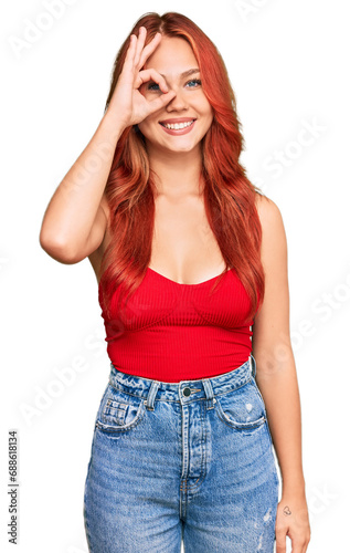 Young redhead woman wearing casual clothes doing ok gesture with hand smiling, eye looking through fingers with happy face.