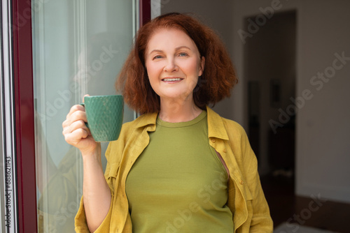 Beautiful senior woman holding cup of tea and smiling at camera