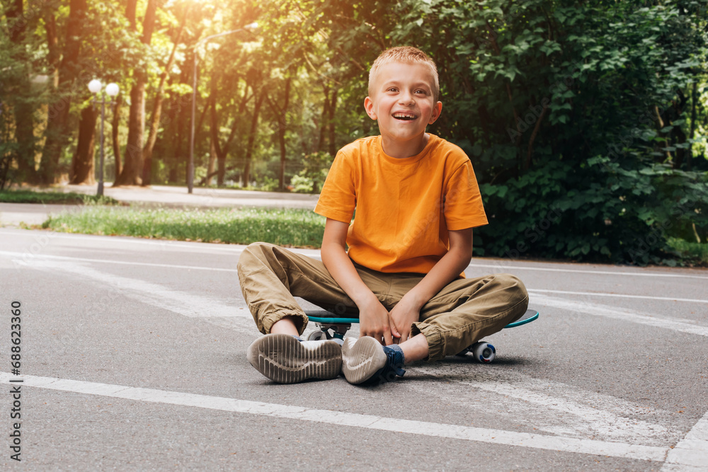 Obraz premium Outdoor activities for children.A cheerful young boy in bright clothes sits on a skateboard. Caucasian schoolboy on a walk. Front view