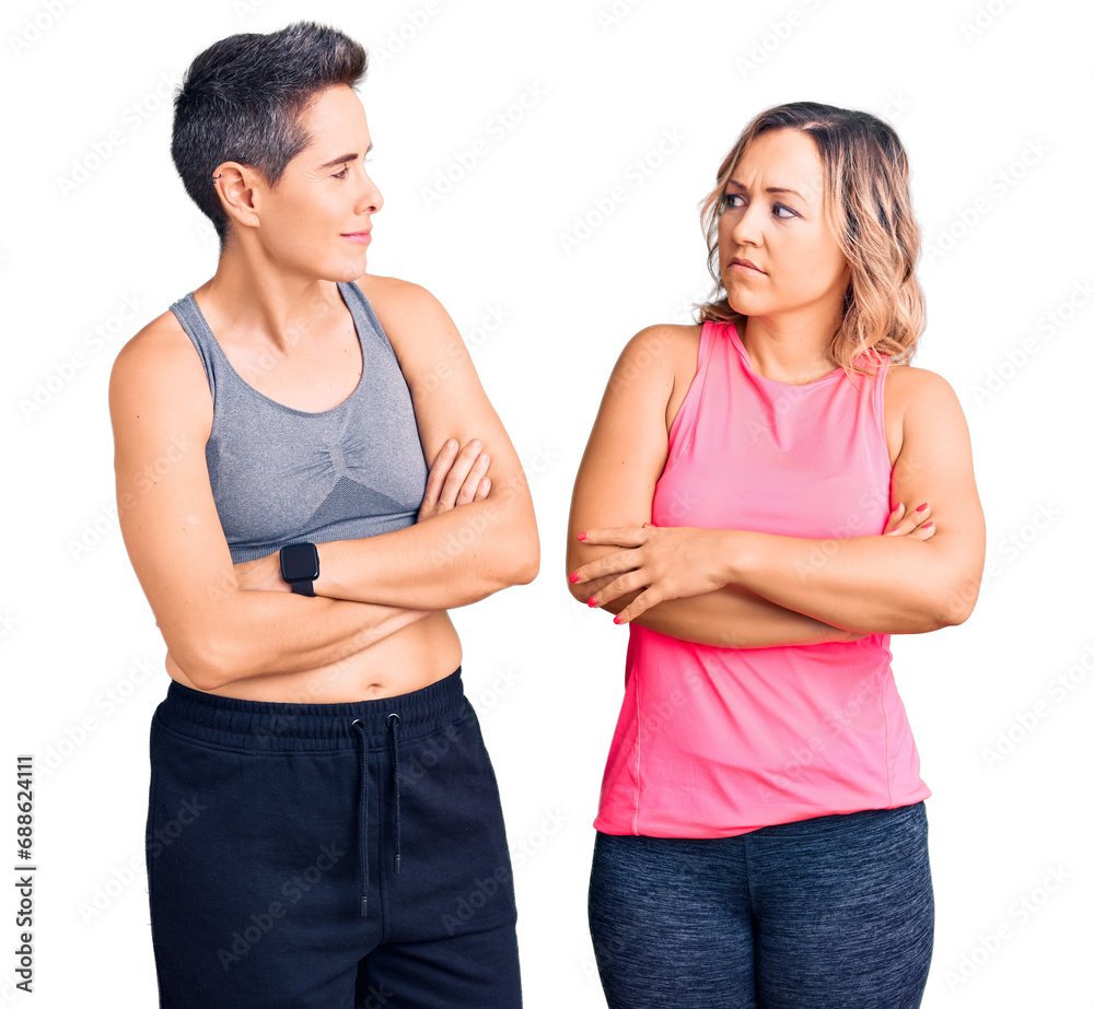 Couple of women wearing sportswear looking to the side with arms crossed convinced and confident