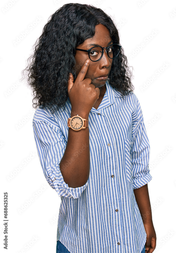 Beautiful african young woman wearing casual clothes and glasses pointing to the eye watching you gesture, suspicious expression Beautiful african young woman wearing casual clothes and glasses pointing to the eye watching you gesture, suspicious expression