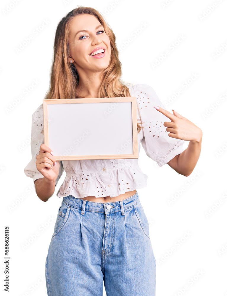 Young caucasian woman with blond hair holding blank empty banner smiling happy pointing with hand and finger Young caucasian woman with blond hair holding blank empty banner smiling happy pointing with hand and finger