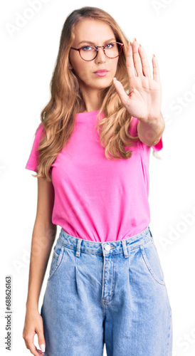 Young beautiful caucasian woman with blond hair wearing casual clothes and glasses doing stop sing with palm of the hand. warning expression with negative and serious gesture on the face. © Krakenimages.com