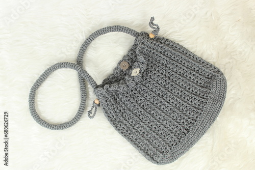 Knitted handmade gray bag on furry white blanket. Top view.