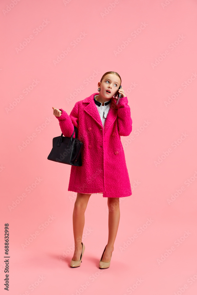 Attractive schoolgirl looks like busy businesswoman, leader taking conversation on phone against pink studio background. Attractive schoolgirl looks like busy businesswoman, leader taking conversation on phone against pink studio background.
